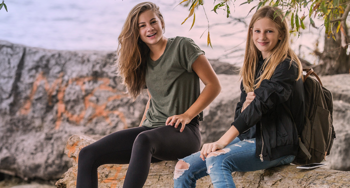 Zwei Mädchen sitzen auf einem Stein und lächeln in die Kamera