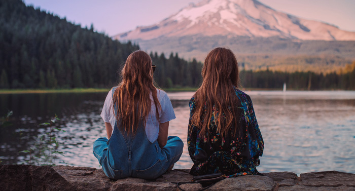 Zwei Mädchen sitzen vor einem See