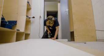 Ein junger Handwerker zersägt Holz auf dem Boden eines leeren Zimmers